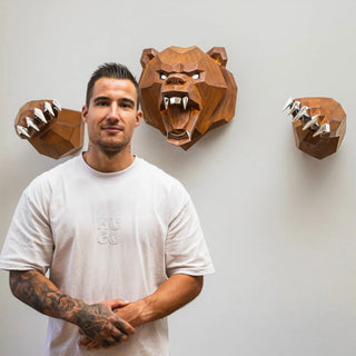 Sculpture murale d'une tête d'ours en métal avec ses deux bras qui sortent du mur fabriquée par l'artiste Cyril Maire, cette sculpture est fabriquée en acier corten et les yeux, les dents et les griffes de l'ours sont en inox brillant
