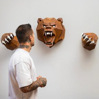 Sculpture murale d'une tête d'ours en métal avec ses deux bras qui sortent du mur fabriquée par l'artiste Cyril Maire, cette sculpture est fabriquée en acier corten et les yeux, les dents et les griffes de l'ours sont en inox brillant