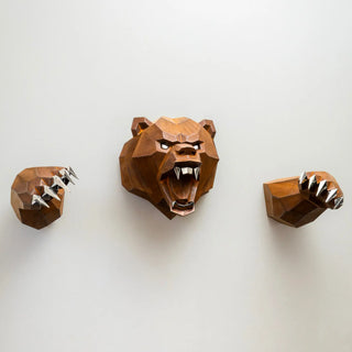 Sculpture murale d'une tête d'ours en métal avec ses deux bras qui sortent du mur fabriquée par l'artiste Cyril Maire, cette sculpture est fabriquée en acier corten et les yeux, les dents et les griffes de l'ours sont en inox brillant