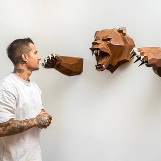 Sculpture murale d'une tête d'ours en métal avec ses deux bras qui sortent du mur fabriquée par l'artiste Cyril Maire, cette sculpture est fabriquée en acier corten et les yeux, les dents et les griffes de l'ours sont en inox brillant
