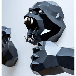 Sculpture murale d'une tête de gorille en métal avec ses deux bras qui sortent du mur fabriquée par l'artiste Cyril Maire, cette sculpture est peinte en noir et les yeux et les dents du gorille sont en inox brillant