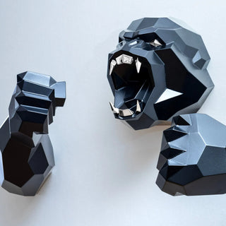 Sculpture murale d'une tête de gorille en métal avec ses deux bras qui sortent du mur fabriquée par l'artiste Cyril Maire, cette sculpture est peinte en noir et les yeux et les dents du gorille sont en inox brillant