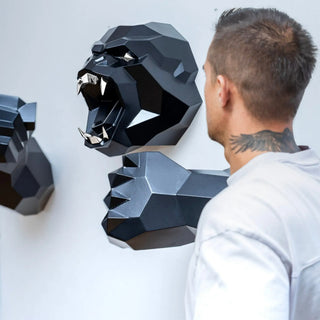 Sculpture murale d'une tête de gorille en métal avec ses deux bras qui sortent du mur fabriquée par l'artiste Cyril Maire, cette sculpture est peinte en noir et les yeux et les dents du gorille sont en inox brillant