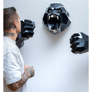 Sculpture murale d'une tête de gorille en métal avec ses deux bras qui sortent du mur fabriquée par l'artiste Cyril Maire, cette sculpture est peinte en noir et les yeux et les dents du gorille sont en inox brillant